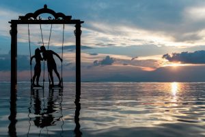 Two people kissing on swings over the ocean